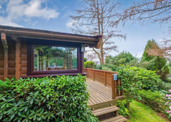 Eine Blockhütte mit großem Fenster, einer Holzterrasse und üppigem Grün.