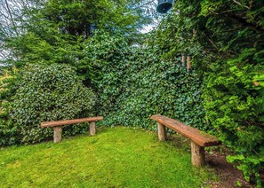 A garden with two wooden benches, lush green foliage, and a hanging light fixture.