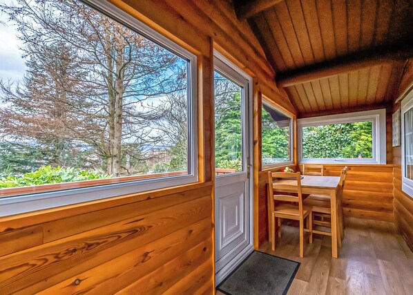 A wooden cabin with large windows, a dining area, and a door leading outside.