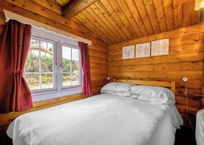 A wooden cabin room with a bed, a window with curtains, and leaf-patterned wall art.