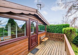 Una terraza de madera con un banco, una puerta y ventanas grandes que dan a un jardín.