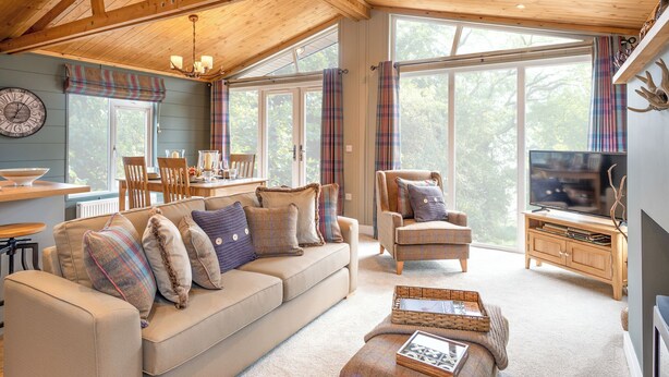 Interior acogedor de una cabaña con techo de madera, un sofá con cojines estampados, un comedor y un televisor.