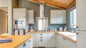 Una cocina compacta con techo de madera, armarios blancos, horno empotrado y ventana con cortinas.