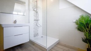 Ein modernes Badezimmer mit Duschkabine aus Glas, einem weißen Waschtisch mit Schubladen und einer Topfpflanze.
