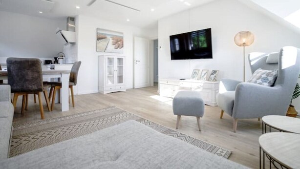 Ein modernes Wohnzimmer mit Essbereich, einem an der Wand befestigten Fernseher und einem großen Fenster, das natürliches Licht hereinlässt.