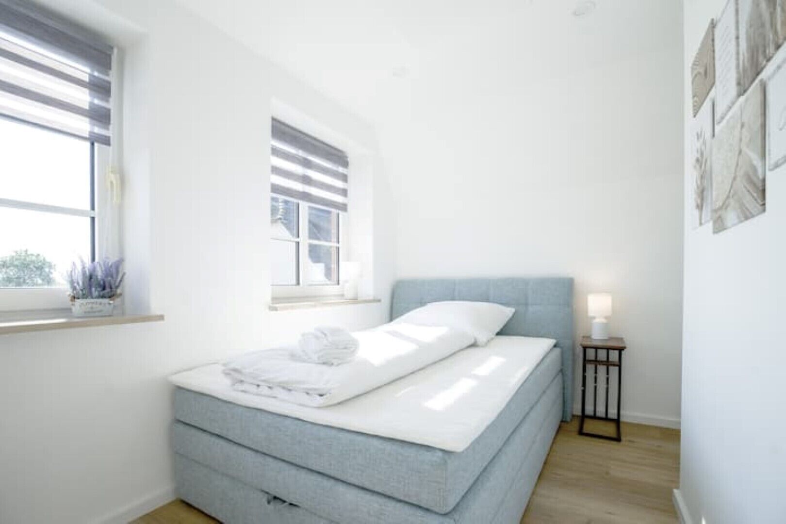 A bedroom with a bed, a bedside table, a window, and a wall-mounted artwork.