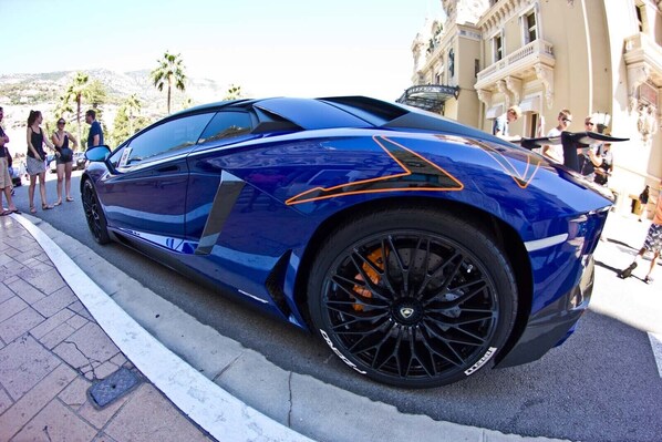 A blue sports car parked on a city street with palm trees and buildings in the background.