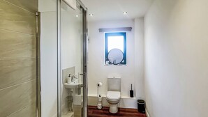 Een badkamer met een douchecabine van glas, een wastafel, een toilet en een raam.