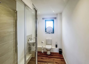 Un baño con mampara de vidrio, lavamanos, inodoro y ventana.