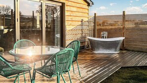 Een houten terras met een glazen tafel en stoelen, een jacuzzi en een houten omheining.