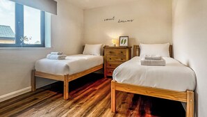 Een slaapkamer met twee eenpersoonsbedden, een dressoir, een bedlampje, een ingelijst schilderij en een raam met uitzicht.