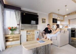 Een moderne woonkamer met een bank, een salontafel, een flatscreen televisie, een keukenhoek en een eettafel.