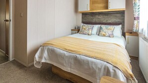 A bedroom with a bed, a wardrobe, a nightstand, and a window with curtains. - 3 bedroom accommodation in Holywell Bay (Holywell Bay)