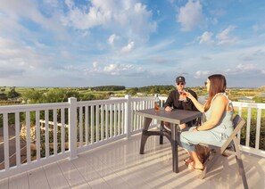 Eine Terrasse mit weißer Brüstung, einem Tisch und zwei Personen, die sitzen.