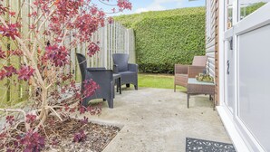 A patio with wicker furniture, a wooden fence, and a green hedge.