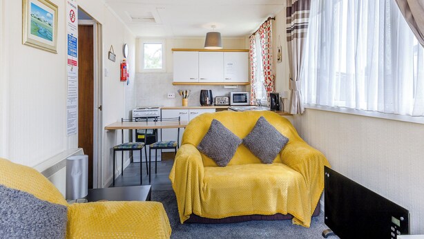 A compact living space with a sofa, a dining table, a kitchenette, and a window with curtains.
