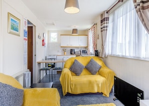 Een ruimtelijk ingerichte leefruimte met een bank, een eettafel, een kitchenette en een raam met gordijnen.