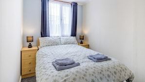 A bedroom with a bed, two bedside tables, a window with curtains, and a ceiling light.