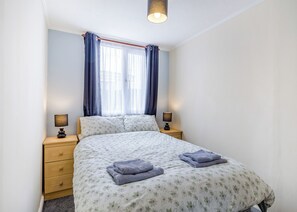 Een slaapkamer met een bed, twee nachtkastjes, een raam met gordijnen en een plafondlamp.