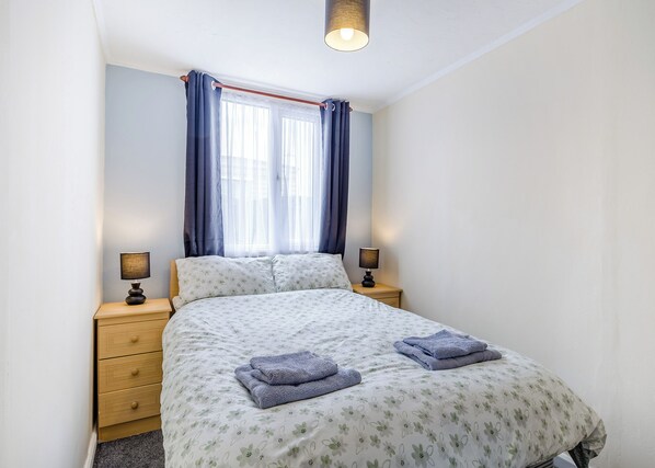 A bedroom with a bed, two bedside tables, a window with curtains, and a ceiling light.