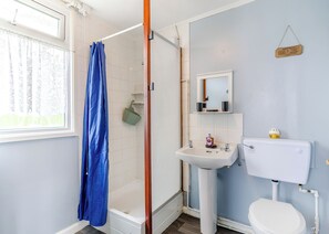 Une salle de bain avec une douche, un lavabo, des toilettes et une fenêtre avec des rideaux.
