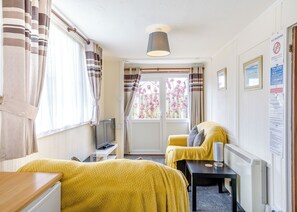 A room with two beds, a TV, a table, a lamp, and a window with curtains.