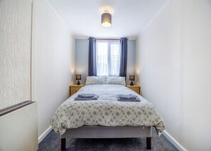 Une chambre à coucher comprenant un lit, deux tables de chevet, une fenêtre avec des rideaux et un luminaire.