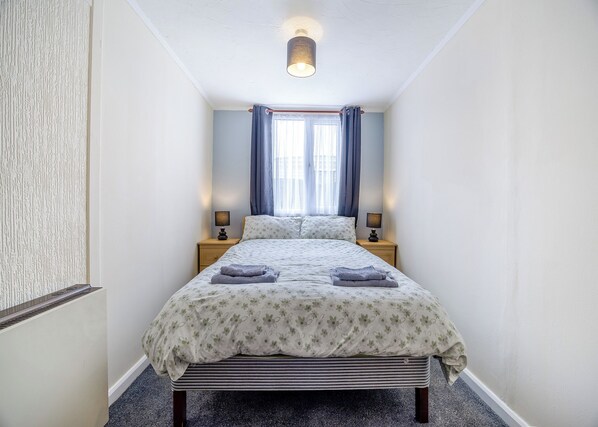 Ein Schlafzimmer mit einem Bett, zwei Nachttischen, einem Fenster mit Vorhängen und einer Lampe.