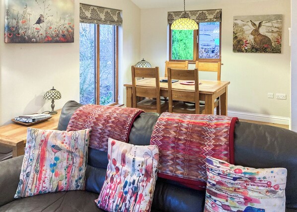 A living room with a sofa, colorful pillows, a dining table with chairs, and artwork on the walls. - 2 bedroom accommodation in Allithwaite (Allithwaite)