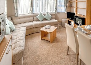 A cozy living room with a sofa, a wooden coffee table, a TV, and a dining area with a table set for two.