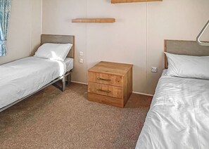 Une chambre avec deux lits simples, une table de chevet en bois et une étagère fixée au mur.