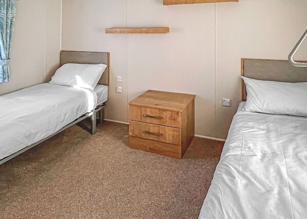 A room with two single beds, a wooden nightstand, and a wall-mounted shelf.