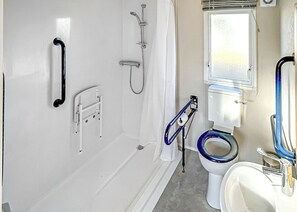 A bathroom with a white bathtub, a shower, a toilet with a blue seat, and a handrail.