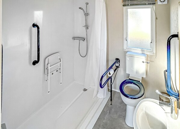 A bathroom with a white bathtub, a shower, a toilet with a blue seat, and a handrail.