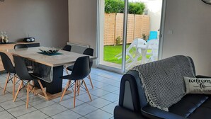 Ein modernes Wohnzimmer mit einer schwarzen Couch, einem Esstisch mit Stühlen und einer Glastür, die zu einem Garten führt.