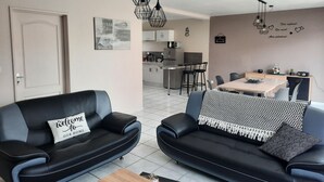 Ein modernes Wohnzimmer mit zwei schwarzen Ledersofas, einem Holztisch und einem Essbereich mit Tisch und Stühlen.