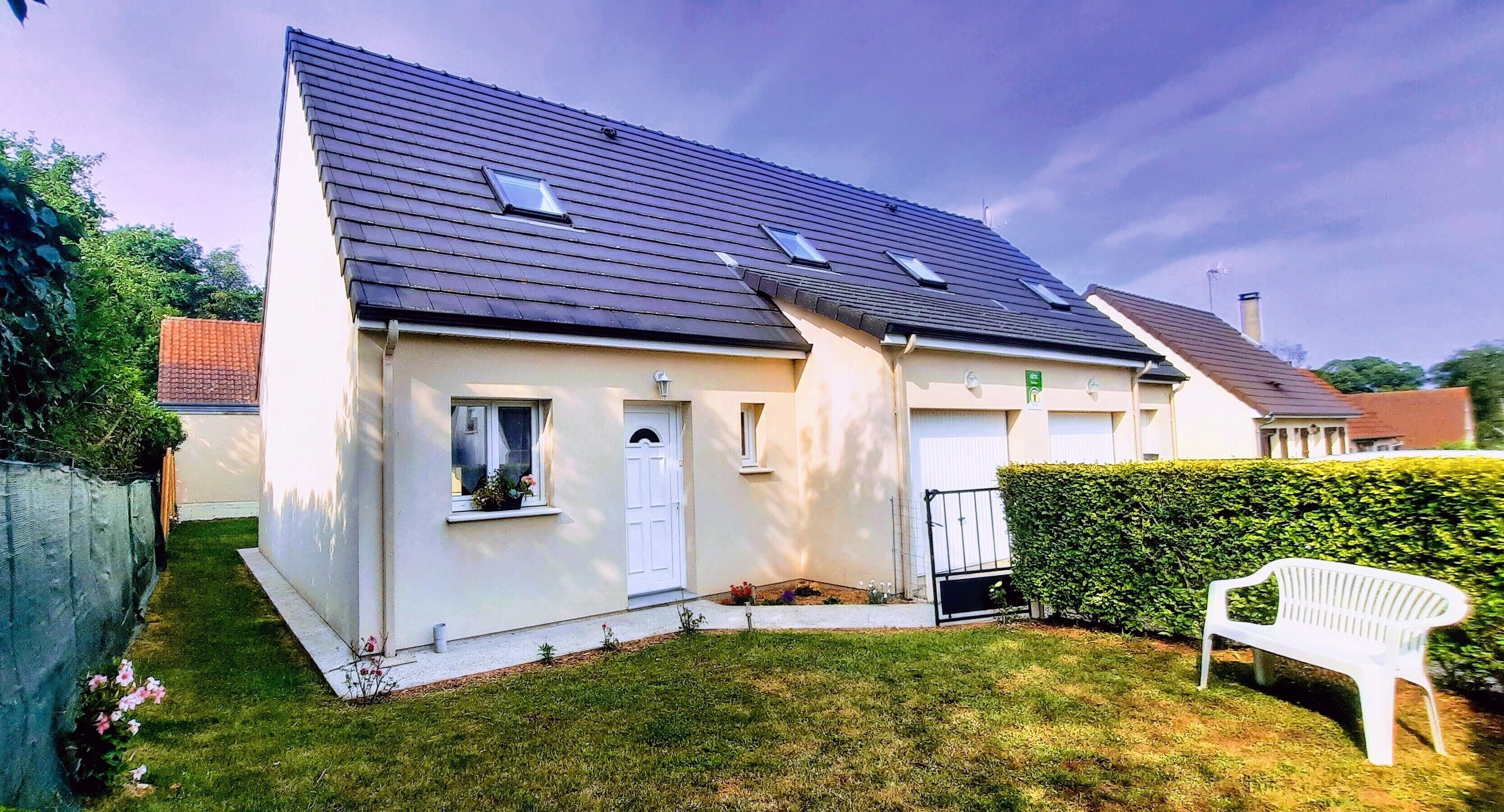 A single-story house with a sloped roof, a front door, and a small front yard with a bench.