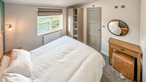Un dormitorio con cama, lámpara de noche, armario, espejo y ventana con vistas.