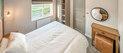 Ein Schlafzimmer mit Bett, Nachttischlampe, Kleiderschrank, Spiegel und einem Fenster mit Blick.