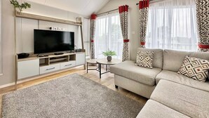 Ein modernes Wohnzimmer mit Flachbildfernseher, einer Couch, einem Couchtisch und einem gemusterten Teppich.