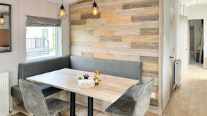 Ein zeitgemäßer Essbereich mit Wandverkleidung aus Holz-Fischgrätparkett, grauen Sitzbänken, einem Holztisch und schwarzen Metallstühlen.