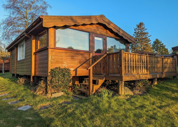 A wooden cabin with a deck, large windows, and a staircase leading to the entrance.