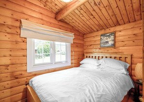 Un dormitorio de cabaña de madera con una cama, una ventana y un cuadro en la pared.