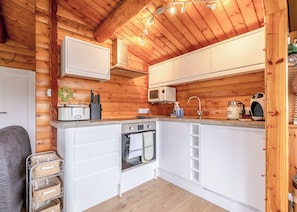 A compact kitchen with wooden walls, white cabinetry, a microwave, a sink, and a stove.