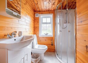 A wooden cabin bathroom with a sink, toilet, and shower.