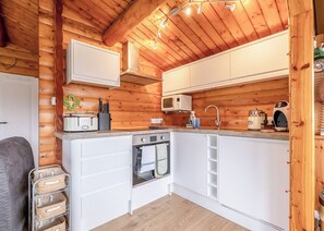 A compact kitchen with wooden walls, white cabinetry, a microwave, a sink, and a stove.