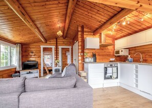 Interior de una cabaña de troncos con sala de estar, kitchenette y un dormitorio con cama elevadas.