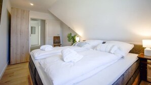 A bedroom with a large bed, a wooden floor, a chair, and a plant. - Kuschelige Küstenlodge Lichtmeer (Nordstrand)