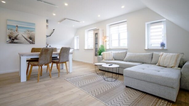 A modern apartment with a dining area, a living room with a sofa, and a kitchen. - Kuschelige Küstenlodge Lichtmeer (Nordstrand)