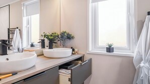 A modern bathroom with two sinks, a mirror, a towel rack, a plant, and a window. - Jura Lodge with Hot Tub (Ayr)